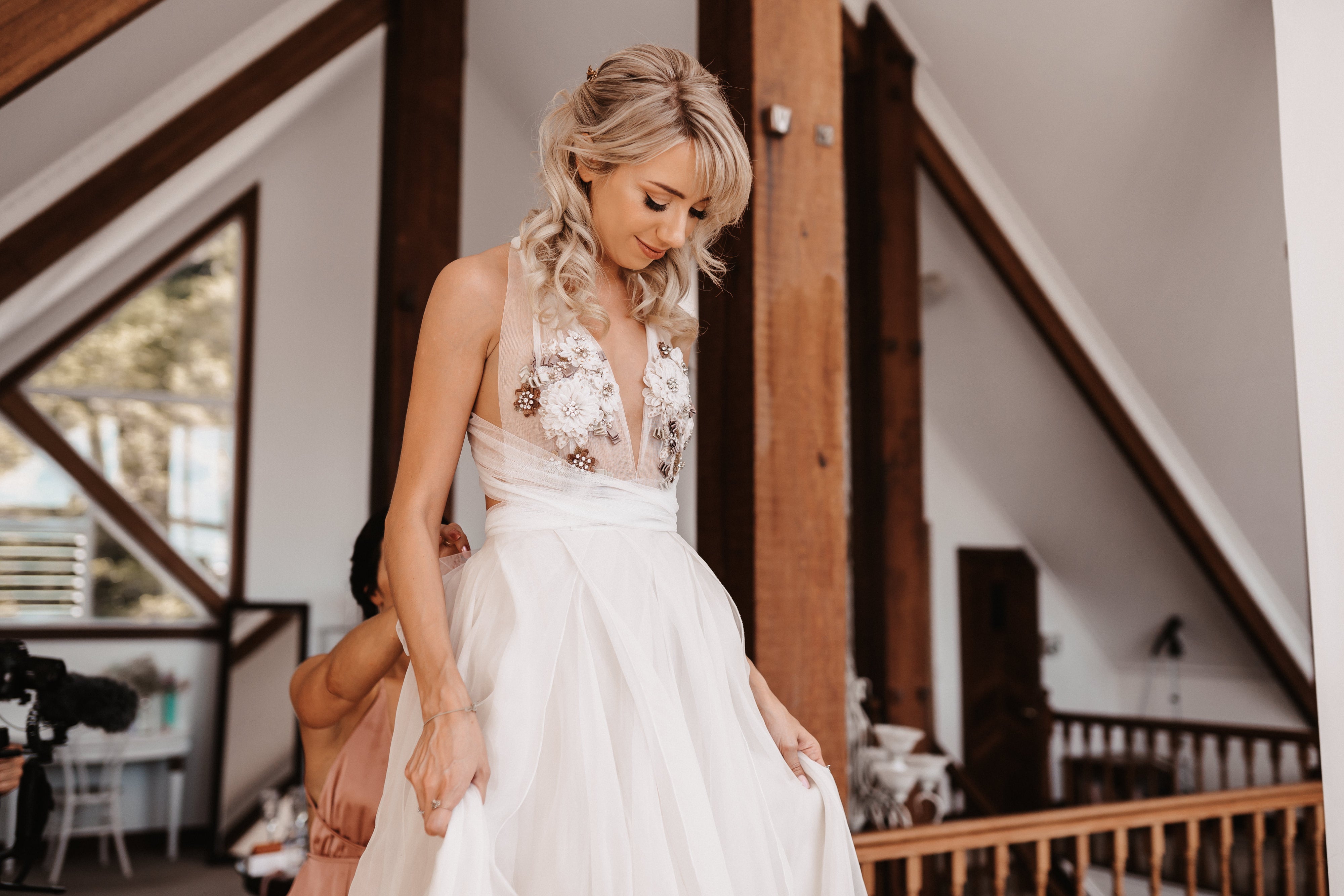 bride in hotel room being fitted into her wedding dress by bridesmaid