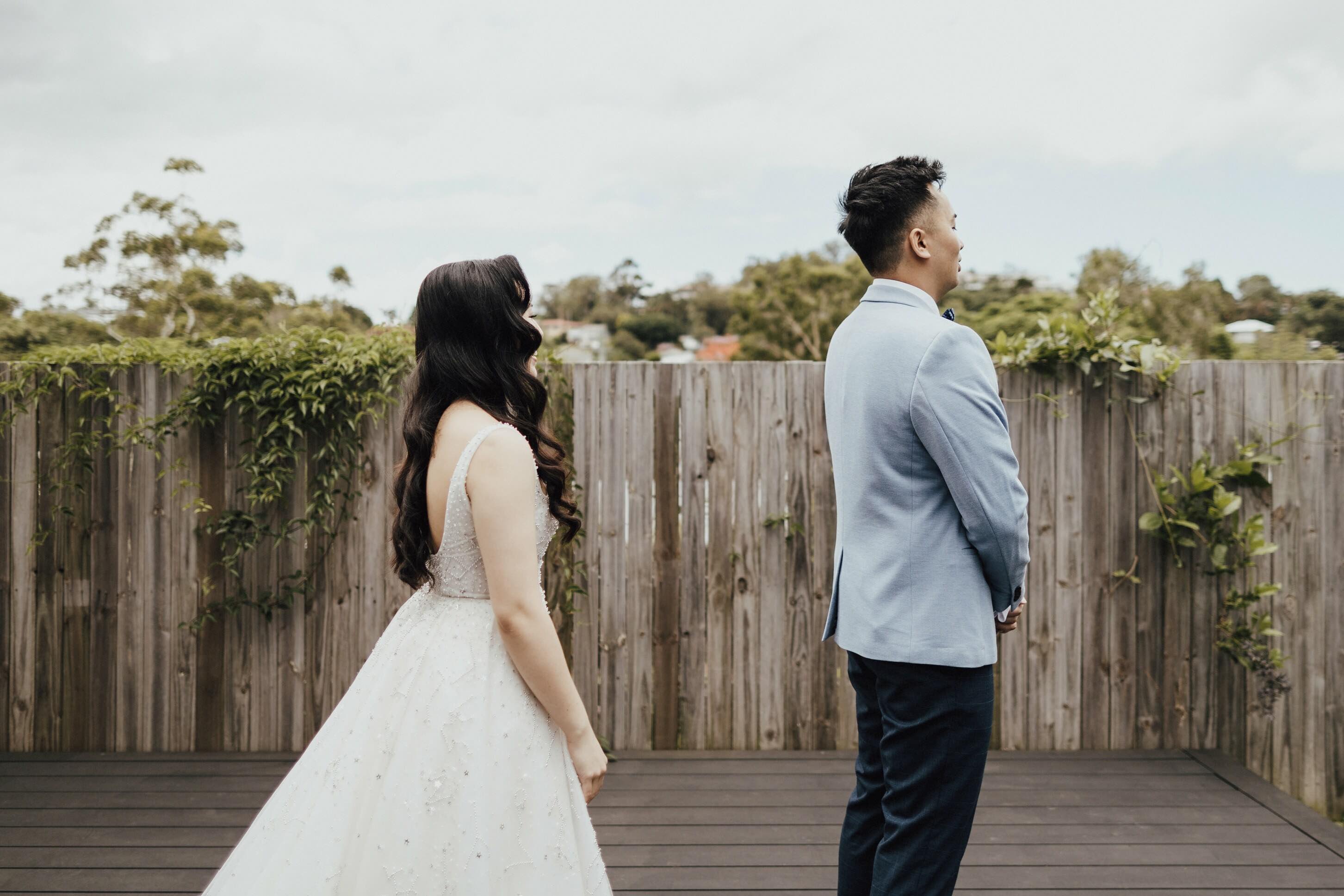 bride in wedding dress standing behind her husband for the first look on wedding day