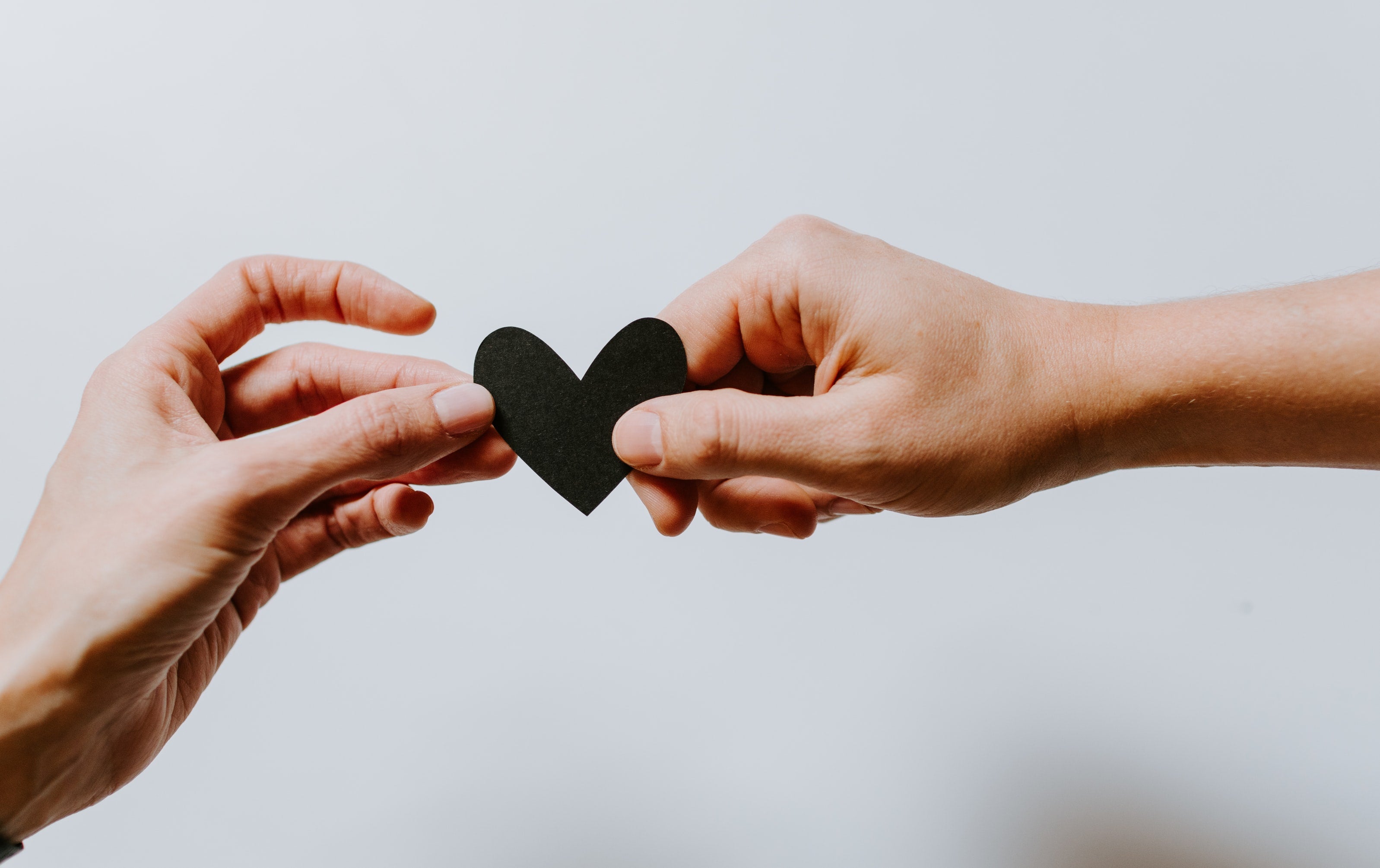 hand passing a black paper heart to another hand