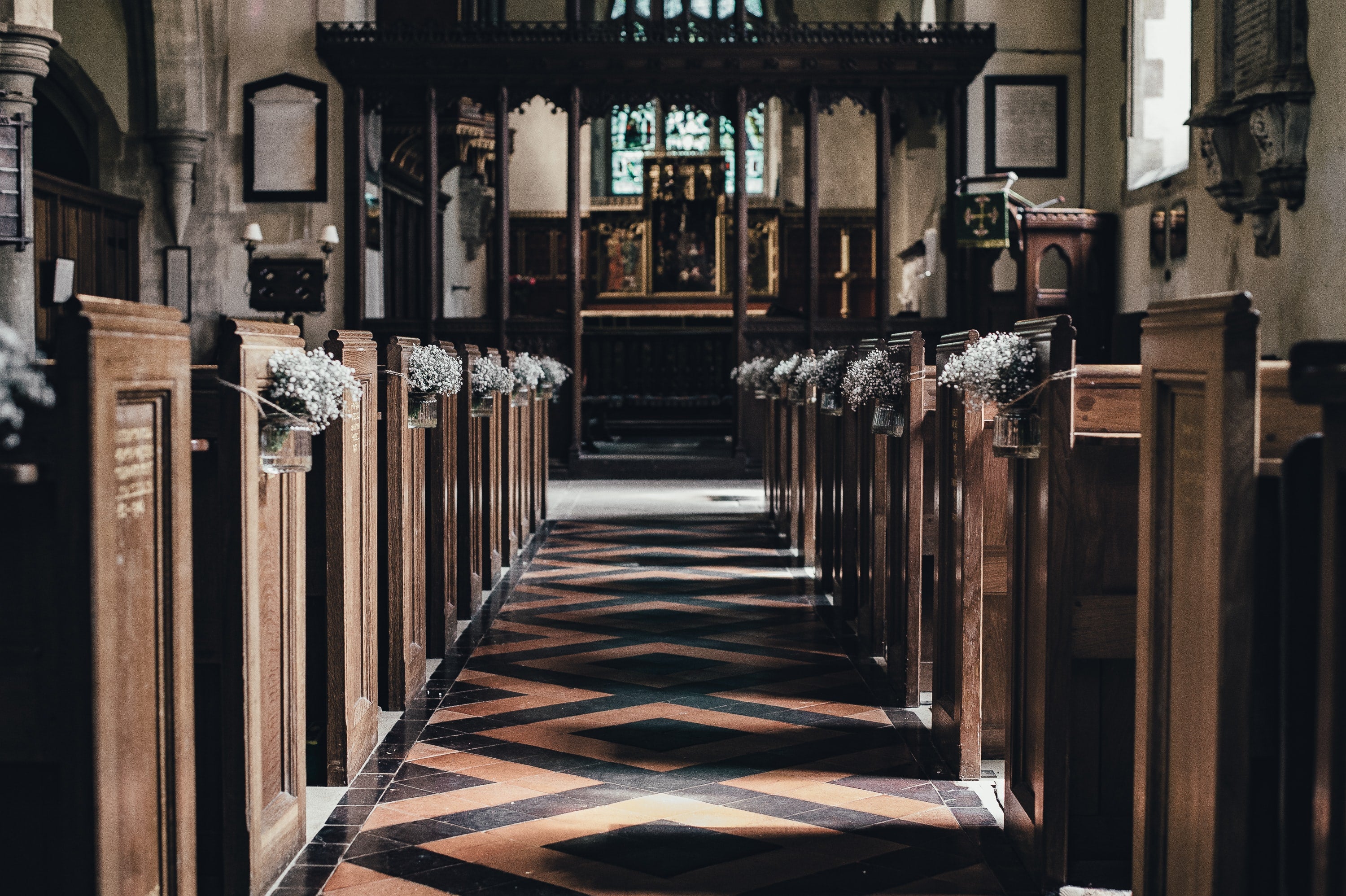 wedding aisle in old church with wooden seats covered by bouquets of wedding flowers