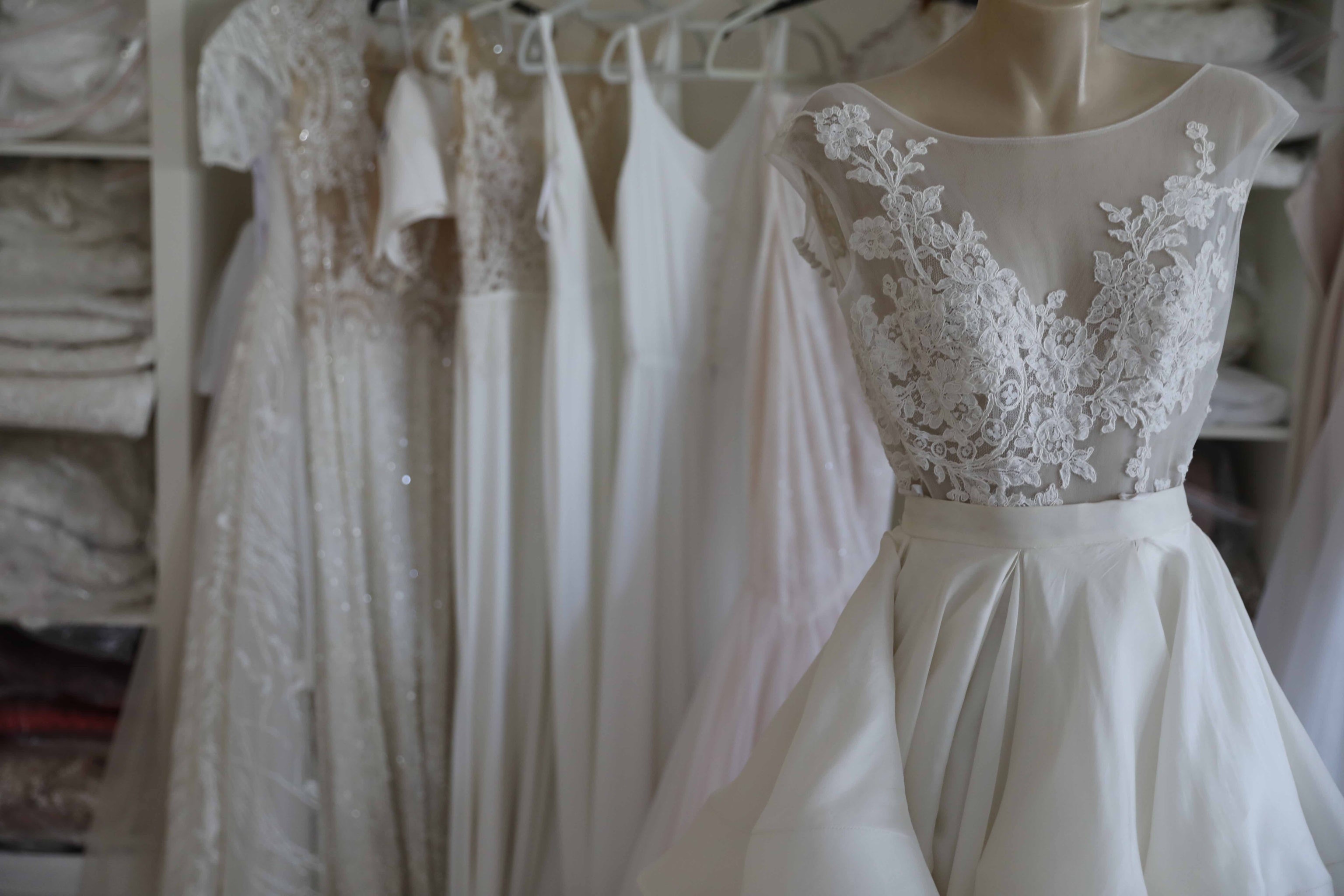 wedding dress on mannequin at bridal store with more wedding gowns on clothing racks in background