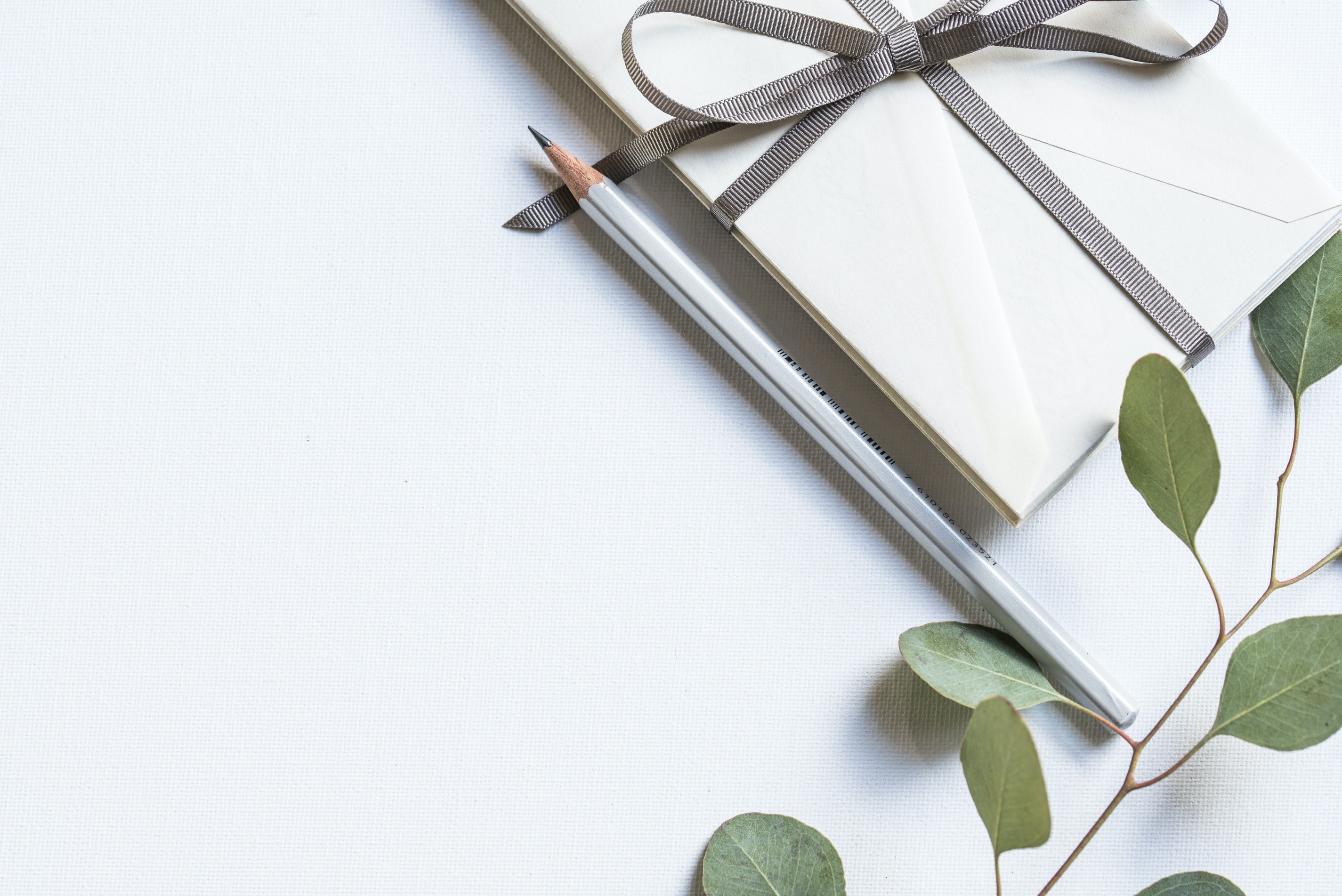 wedding invitations on white fabric with pencil and plant