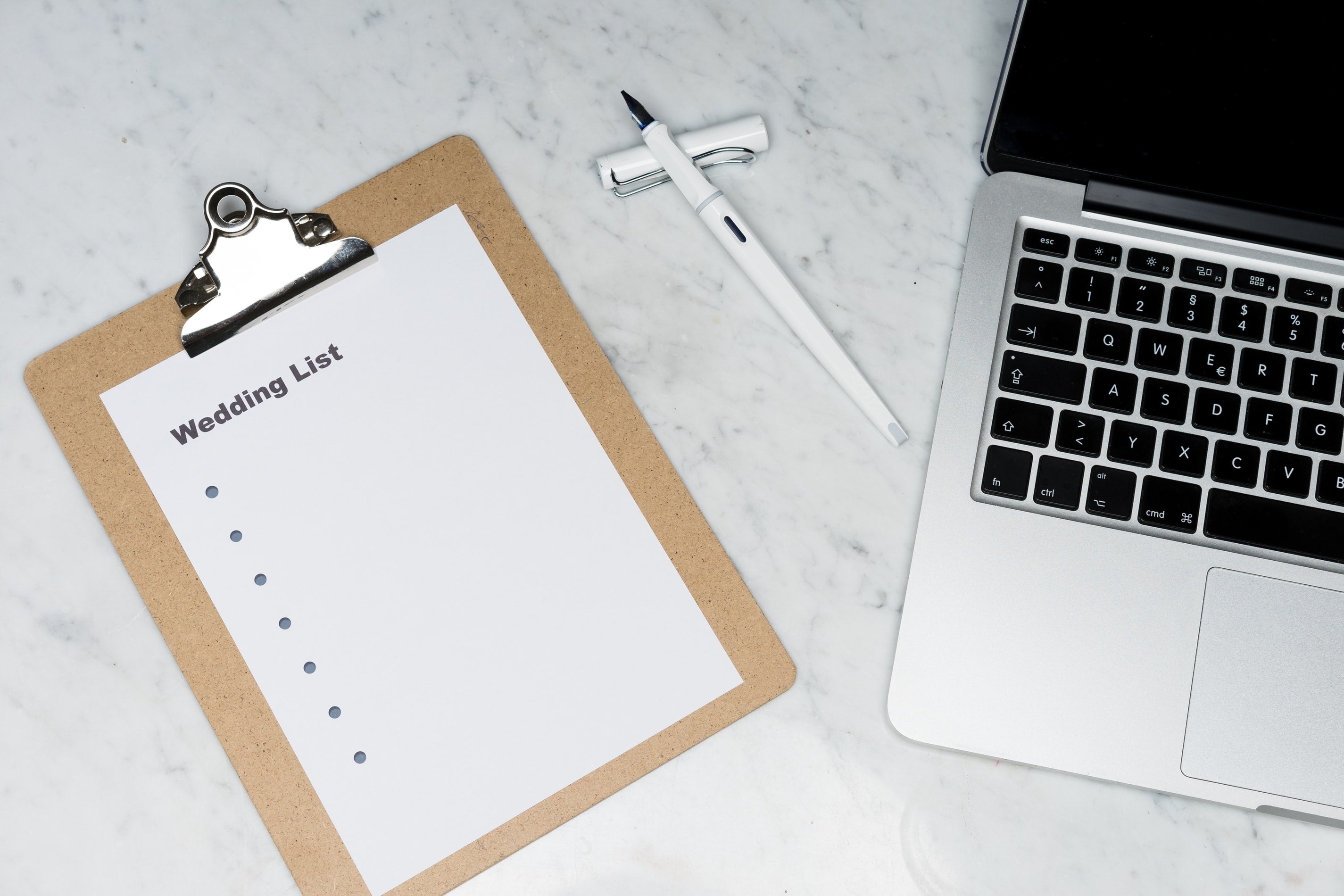 wedding list plus pen and Apple laptop on marble countertop