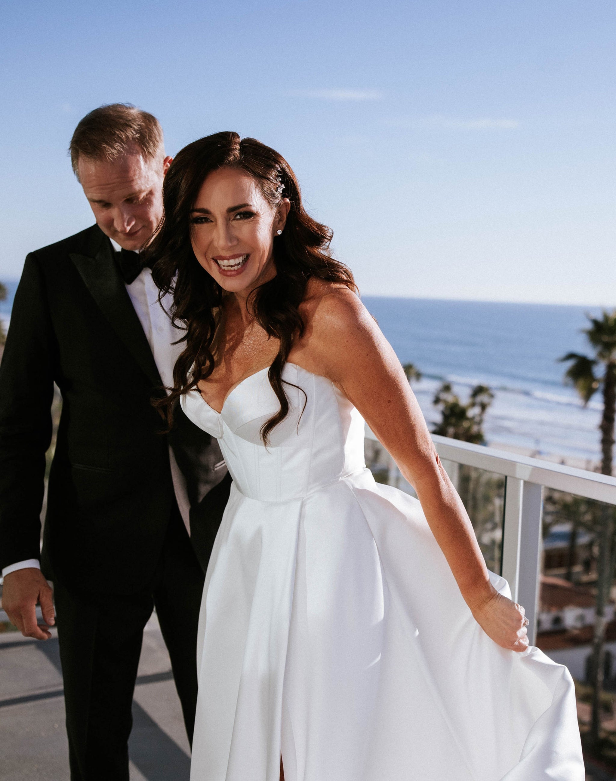 bride in white mikado gown smiling next to husband with beach behind them