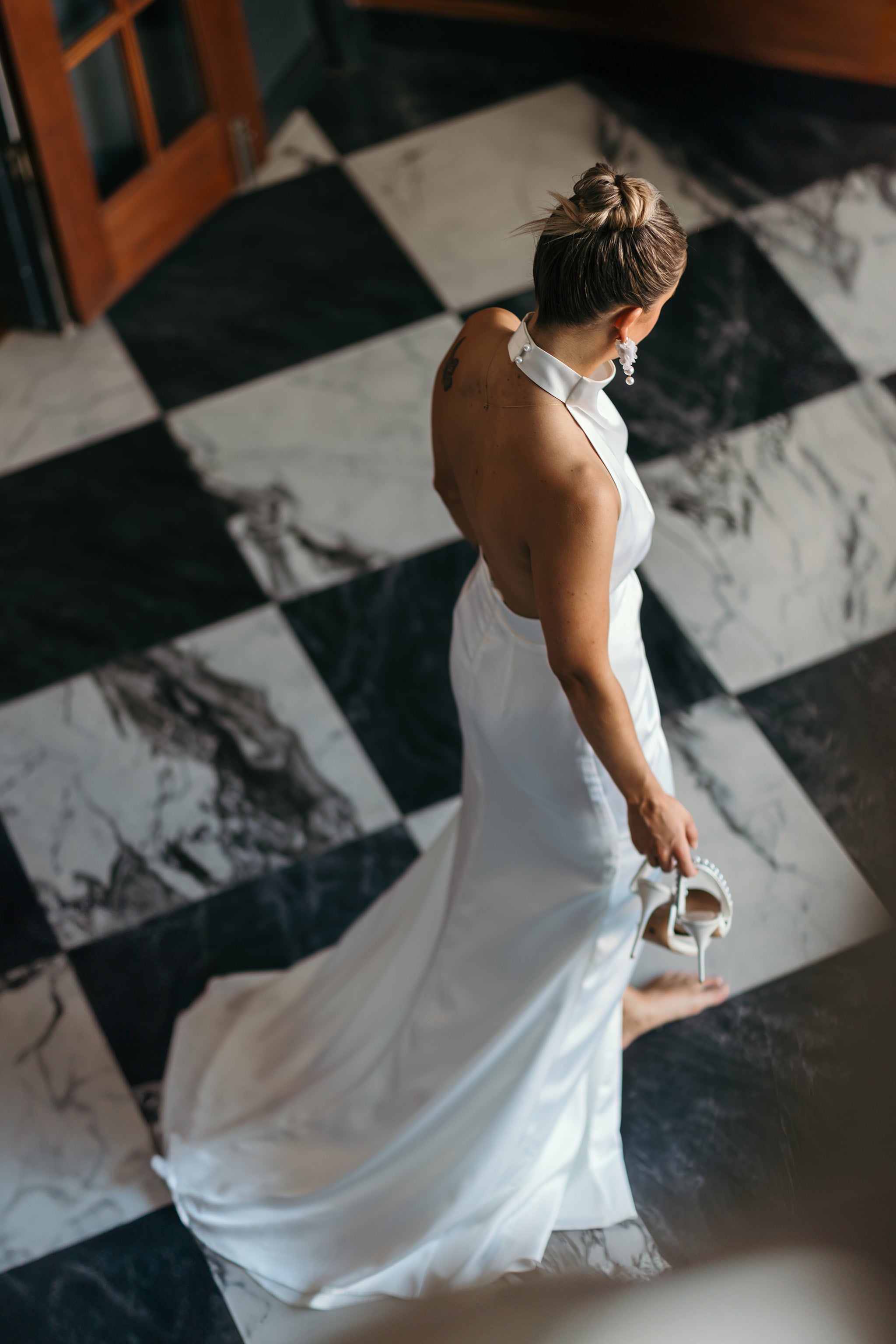 bride walking across checkered floor holding heels