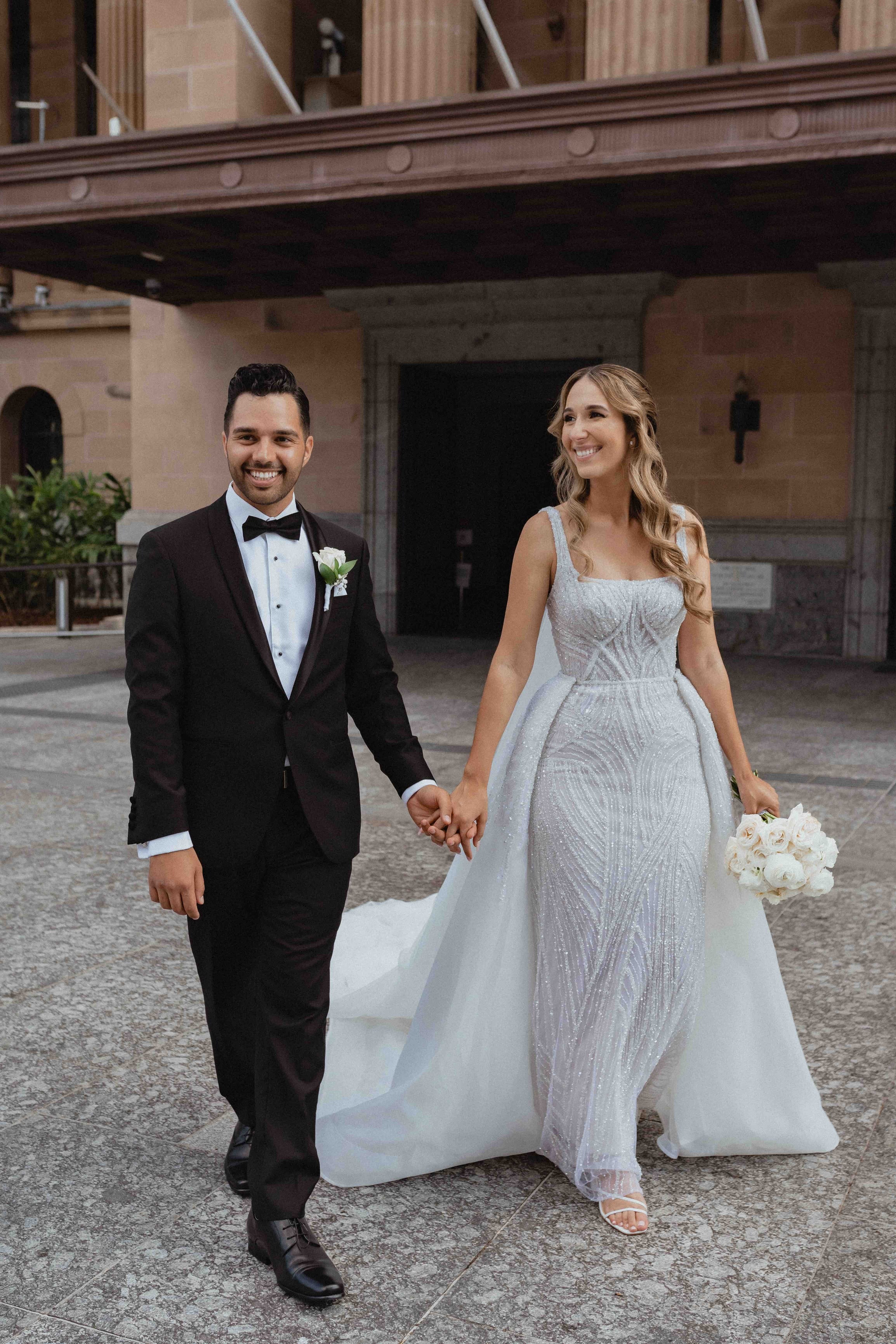 husband and wife in wedding attire walking through city