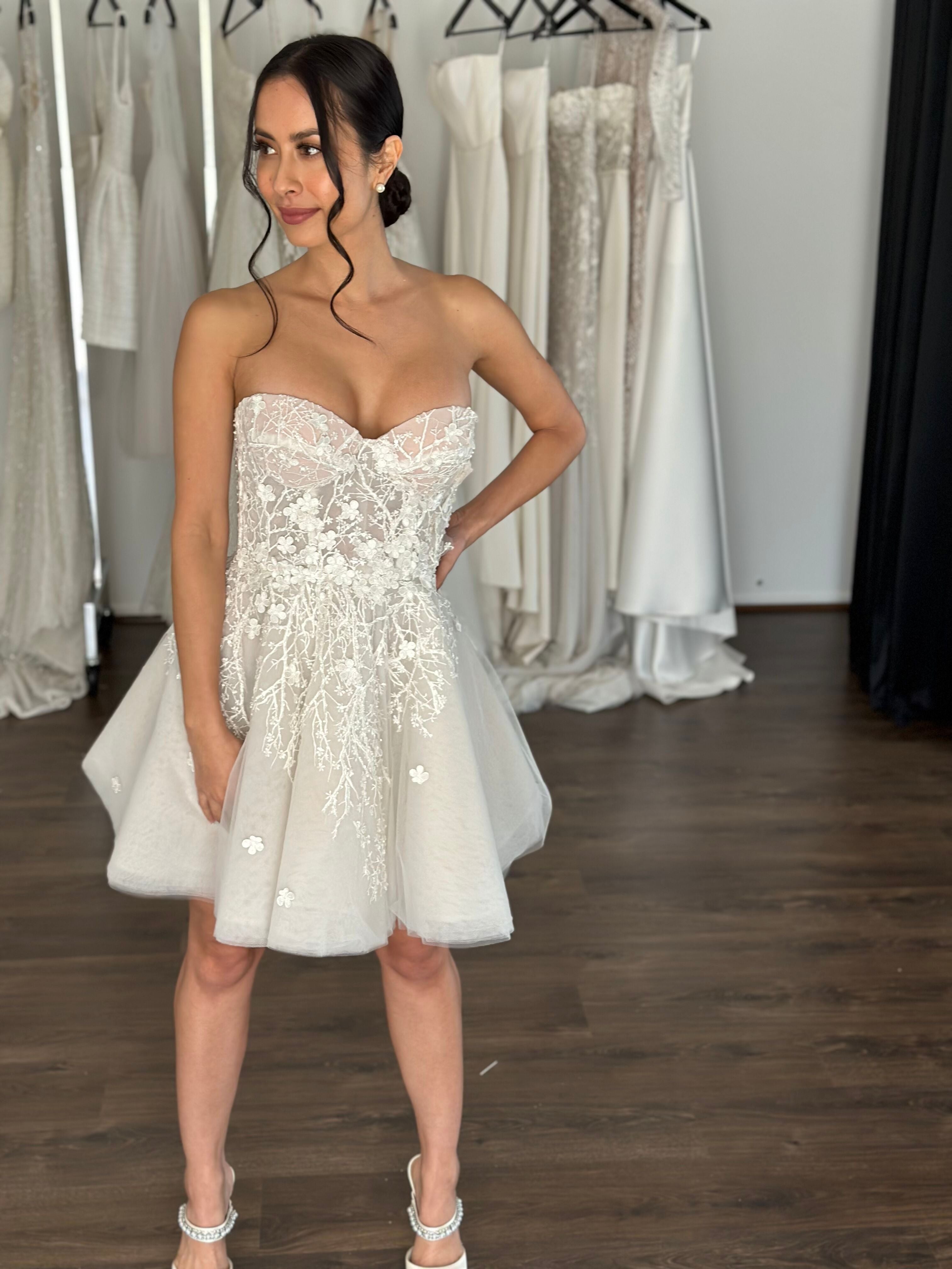 bride wearing mini dress in front of racks of wedding dresses