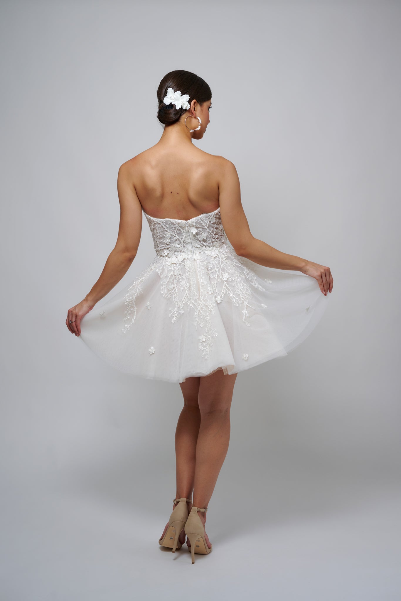 bride with floral hairclip in her air holding the skirt of her mini dress out while posing