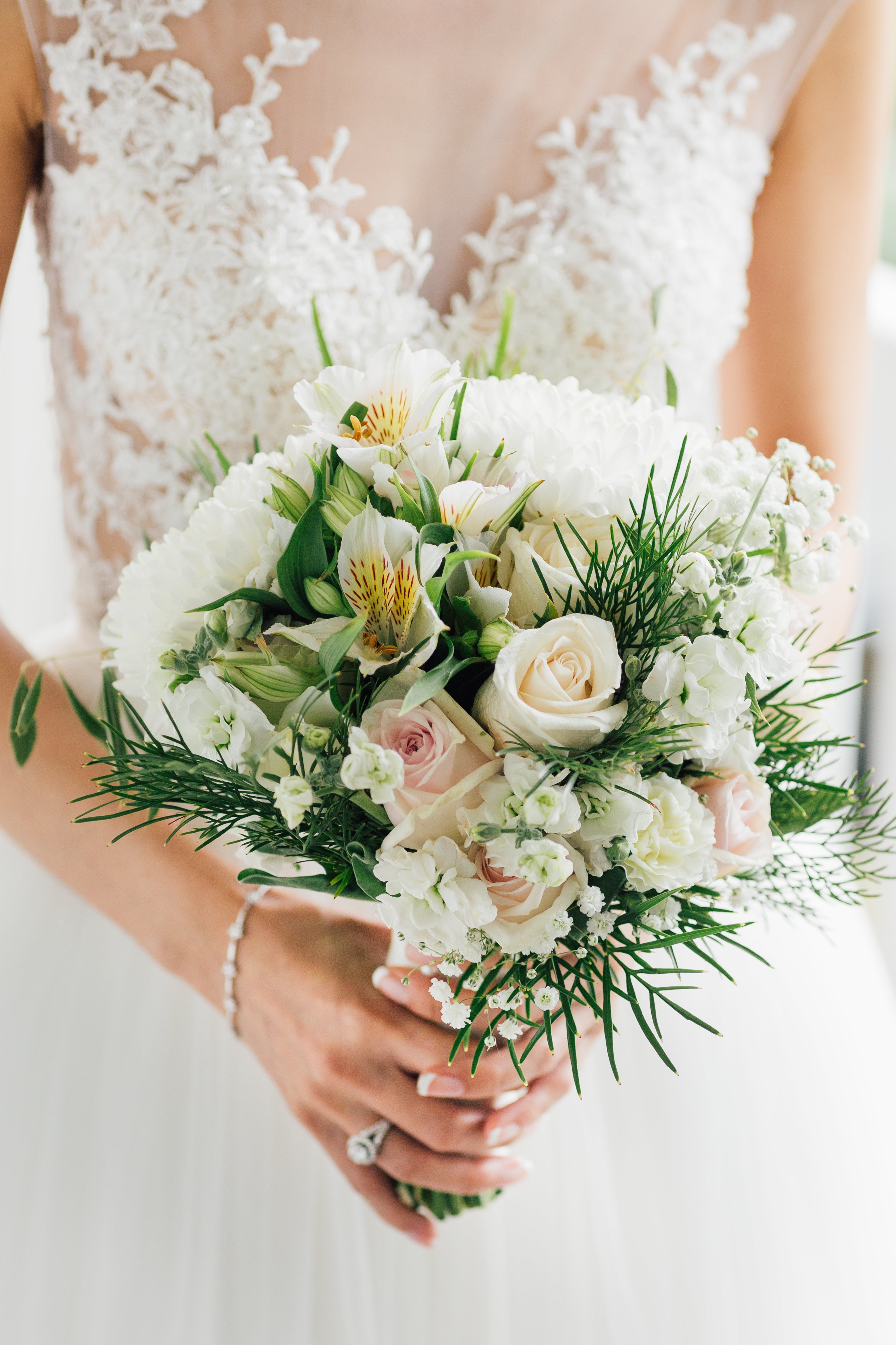 bride in wedding dress made from white lace holding green and white bouquet