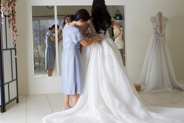 Brisbane wedding dress designer fitting bride into custom wedding gown at bridal studio in front of mirror