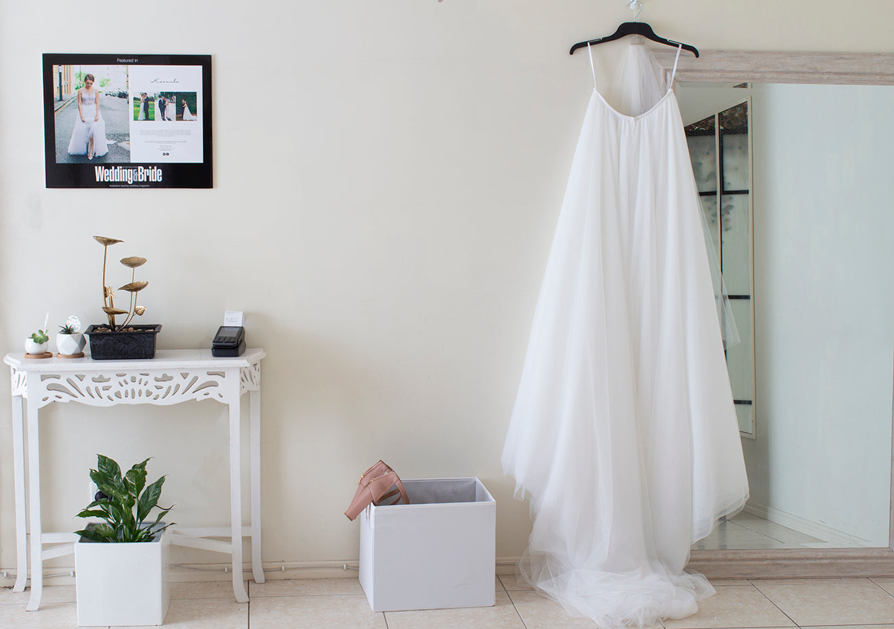 Bridal consult room with a white table featuring an ATM machine, succulent plants, a water feature and a photo hanging above it. To the right of it is a white box and a tall mirror with a white skirt hanging off it