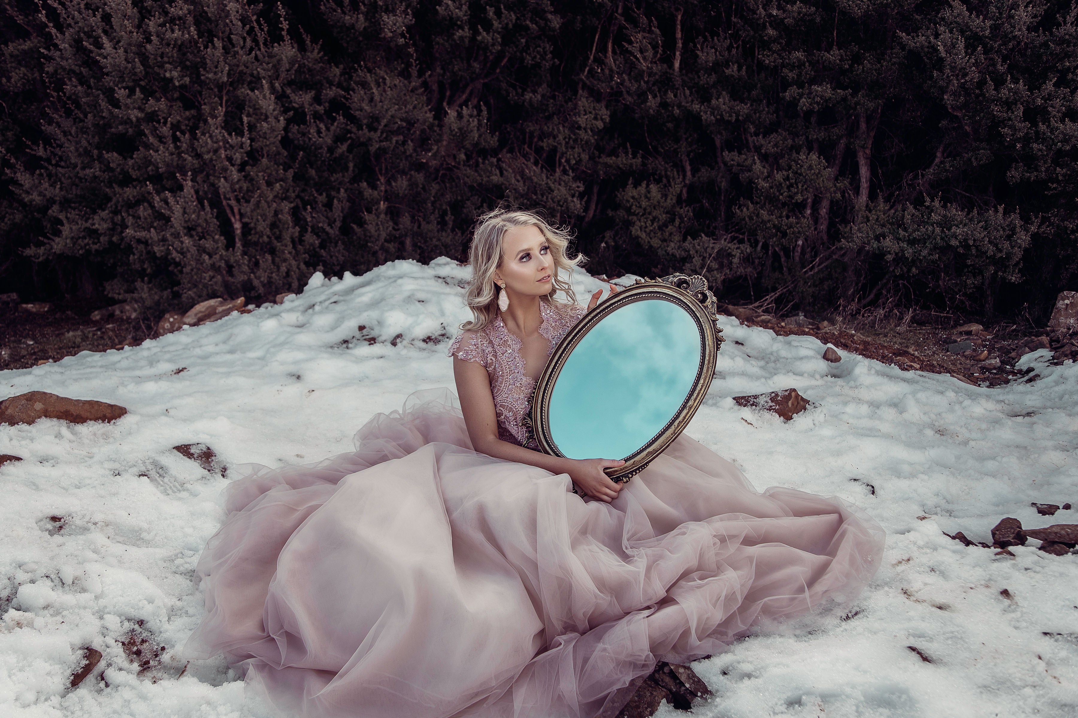Model in pink lace wedding gown holding a mirror to the sky in the snow