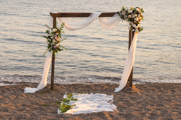beach wedding featuring arch and draped fabric with flowers