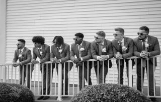 bridal party in suits standing along hand rail