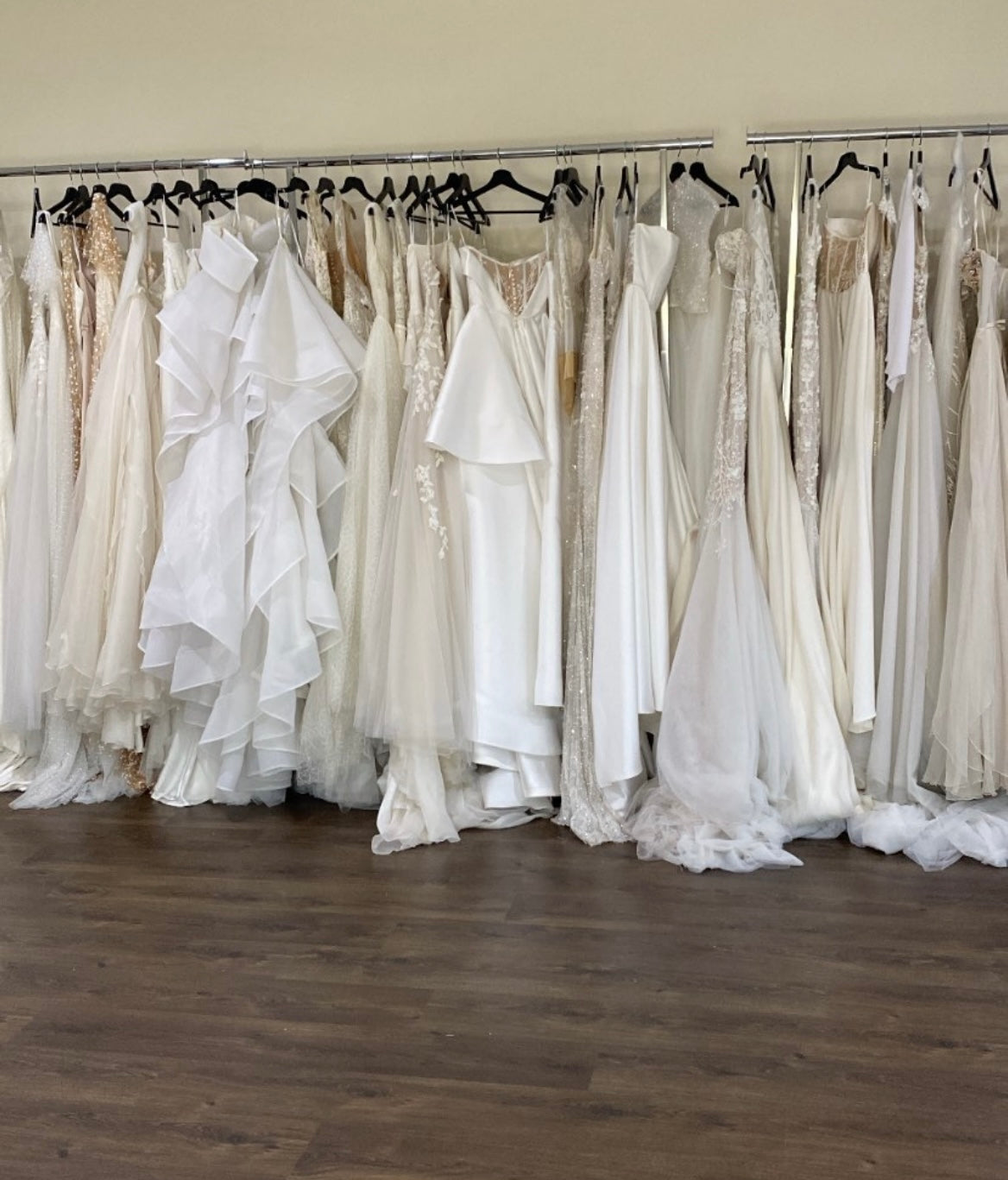 bridal studio with racks full of wedding gowns against white wall with wooden floors