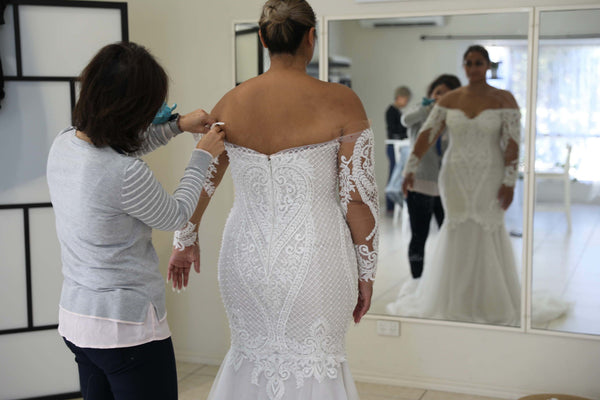 bride having alterations sewn on her wedding dress by woman in front of mirror