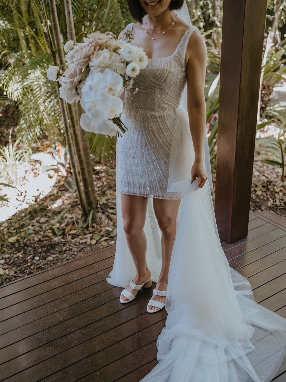 bride in mini reception beaded lace dress and white heels with flowers