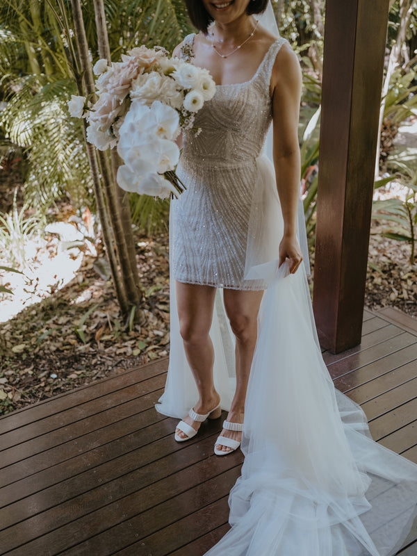 bride in mini reception beaded lace dress and white heels with flowers