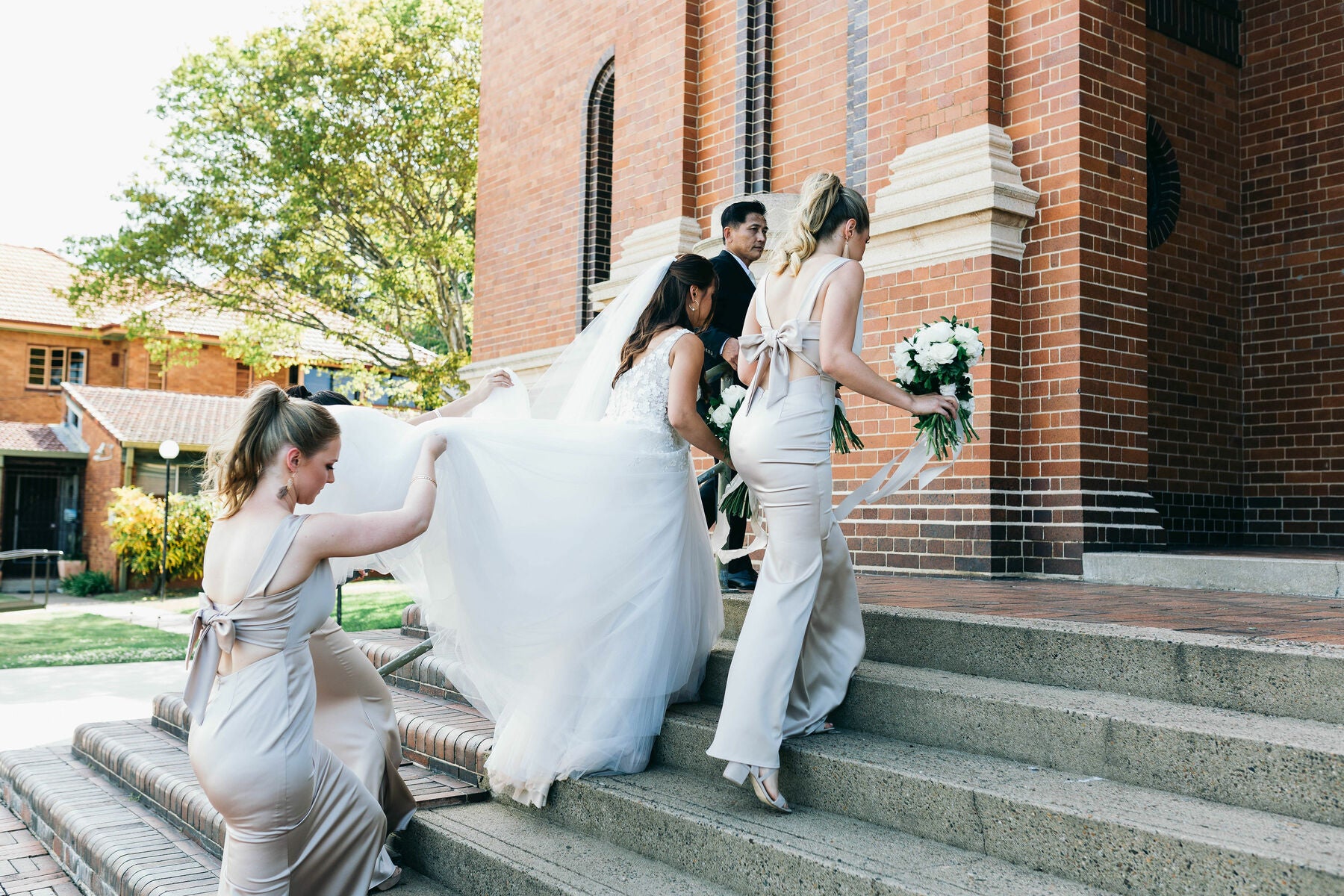 bridesmaids helping bride up the stairs to church on their wedding day