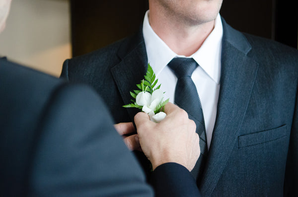groom preparing for wedding ceremony while father places flowers on grooms suit