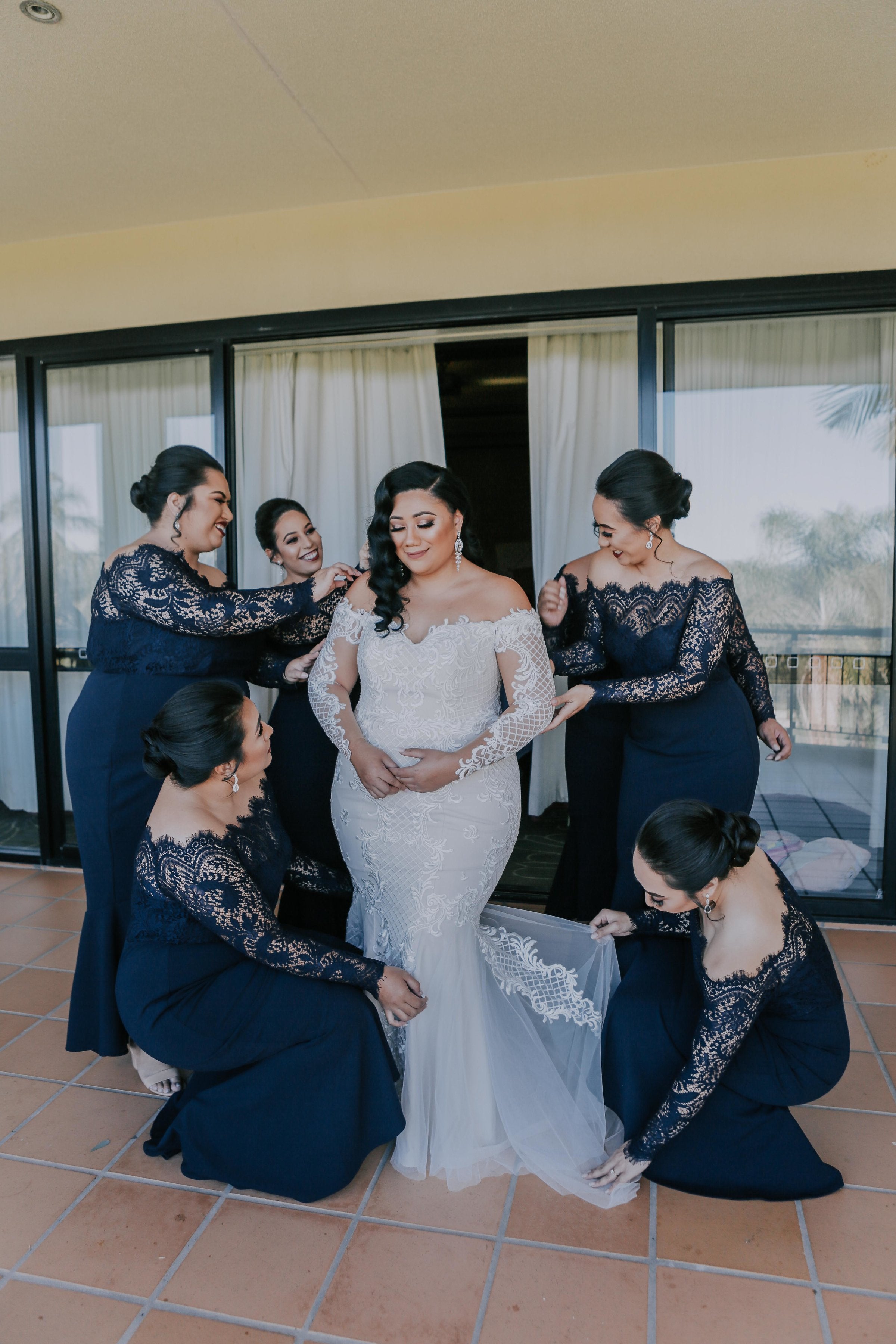 maid of honour and bridesmaids wearing black lace dresses helping bride into her wedding gown