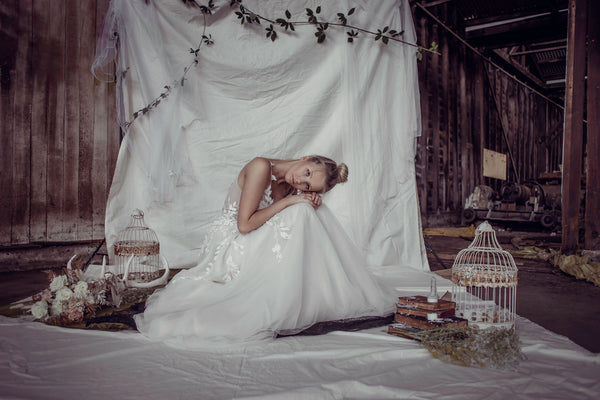 model posing sitting down in a wedding dress surrounded by floral arrangements and a birdcage