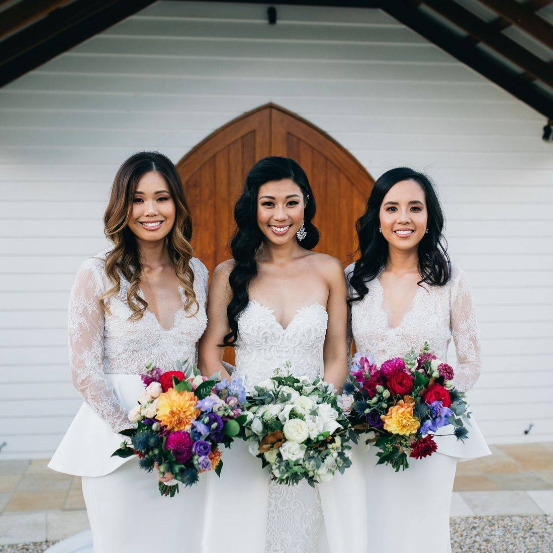 three women in bridal attire holding bouquets of flowers