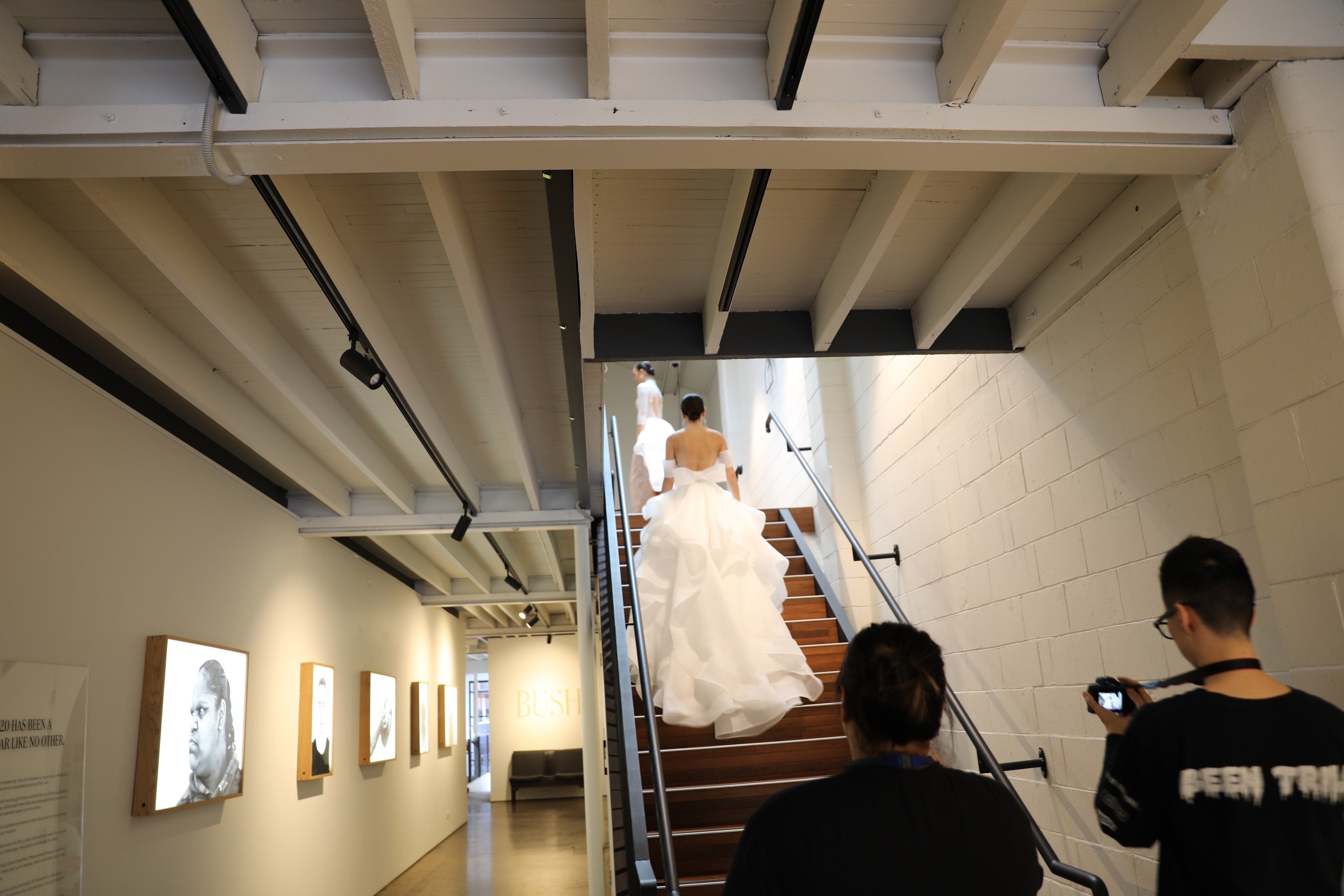 two women in wedding dresses walking up stairs while photographers follow them with cameras