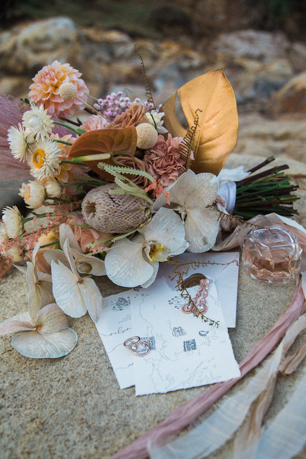 Wedding bouquet with perfume, stationary and wedding rings placed on rock at beach