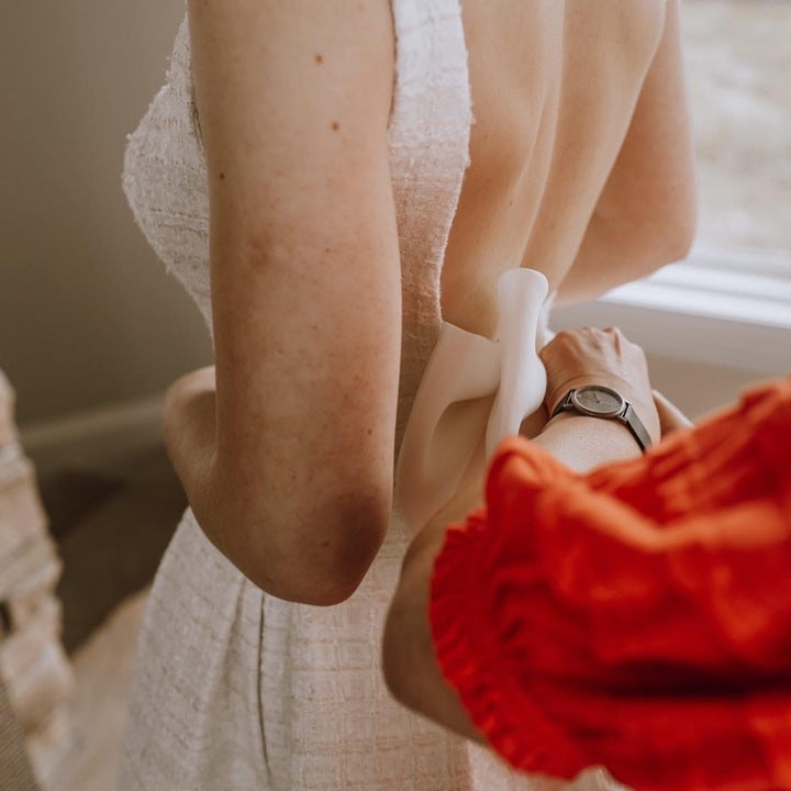 womans hands placing bow on brides wedding dress back