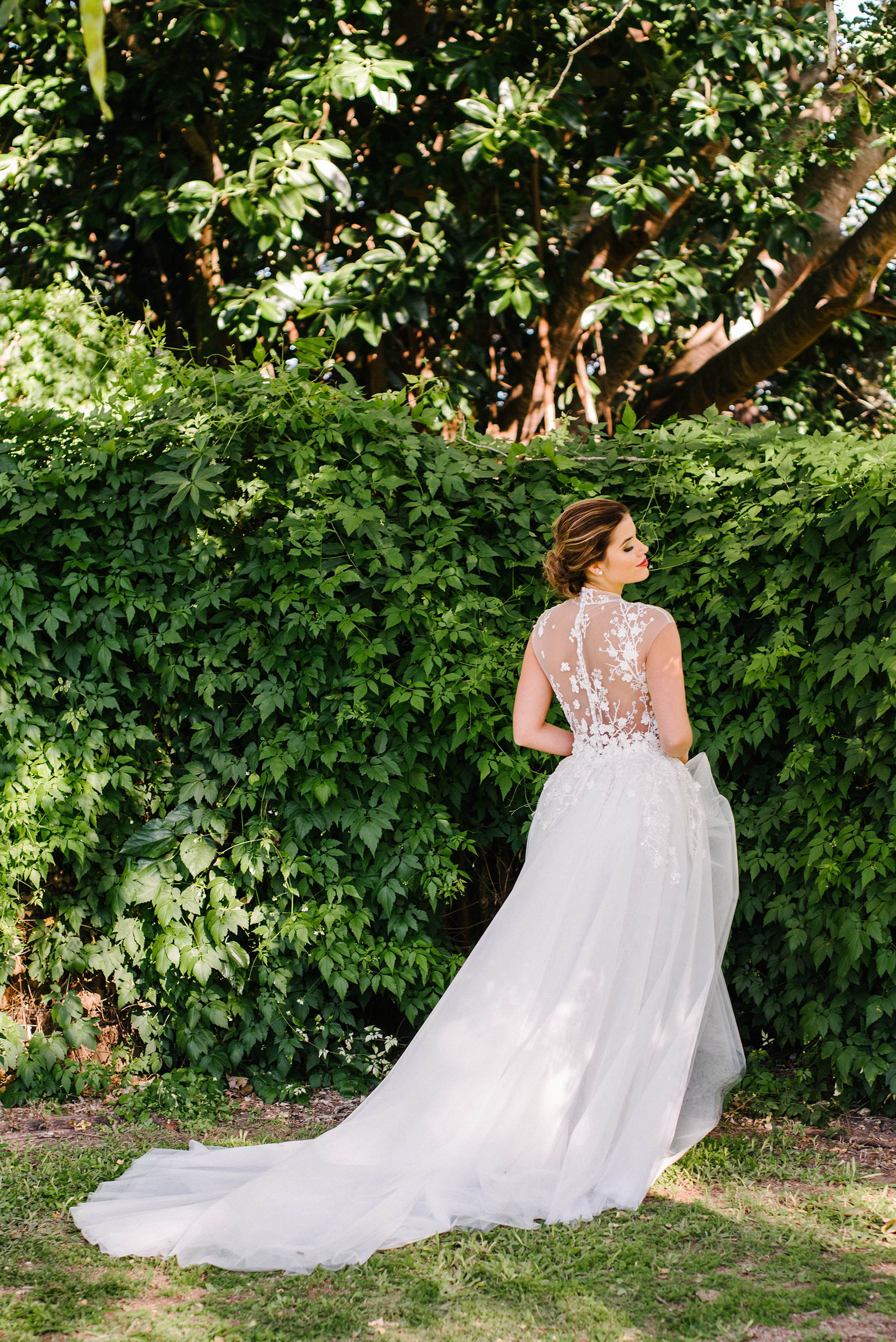 bride standing beside grass wall in wedding dress and outer skirt