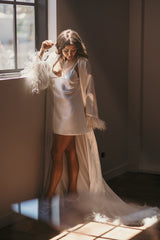 bride standing beside window in her bridal robe and slip