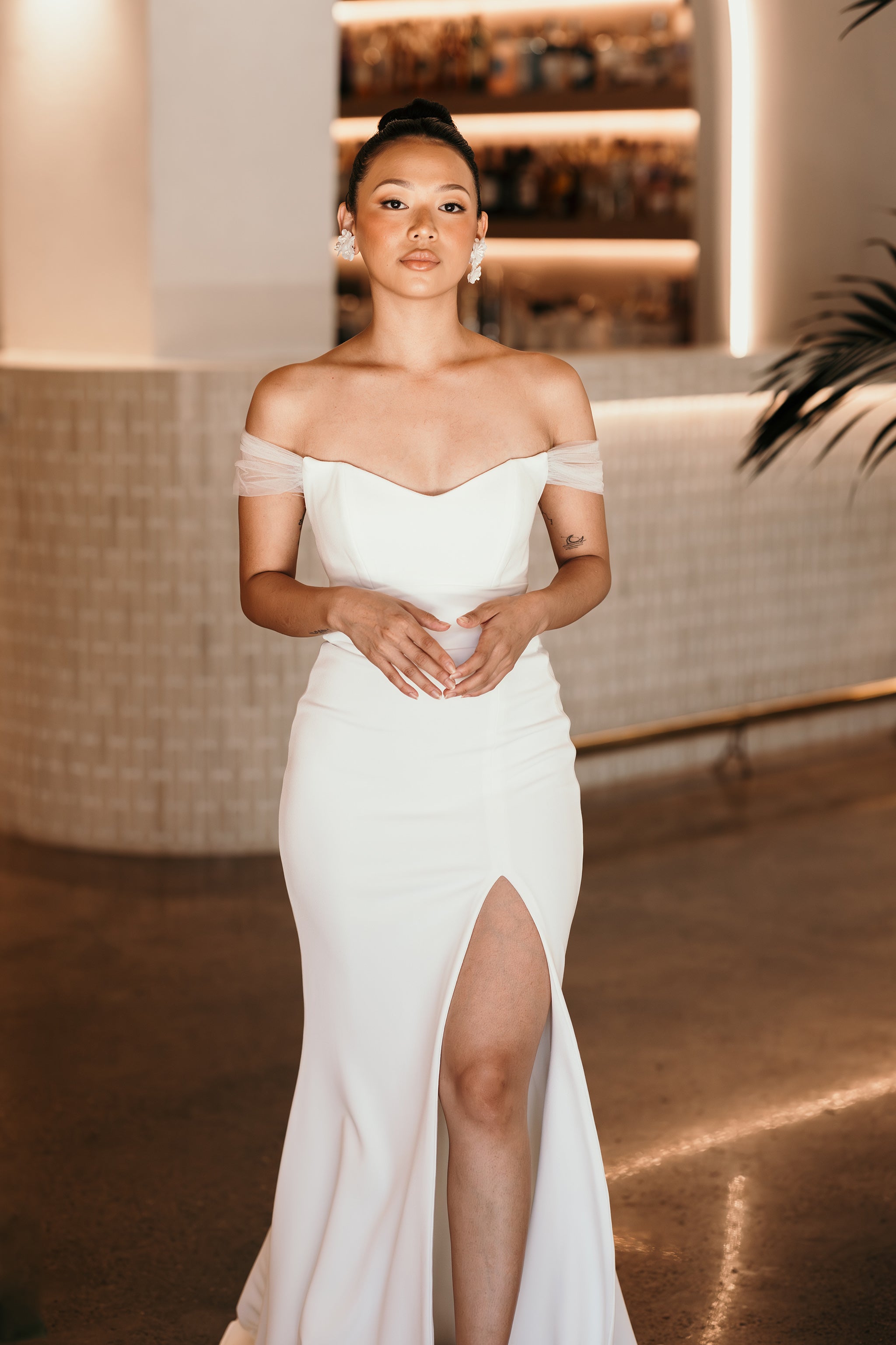 bride standing by the bar in her off the shoulder wedding dress with high thigh split