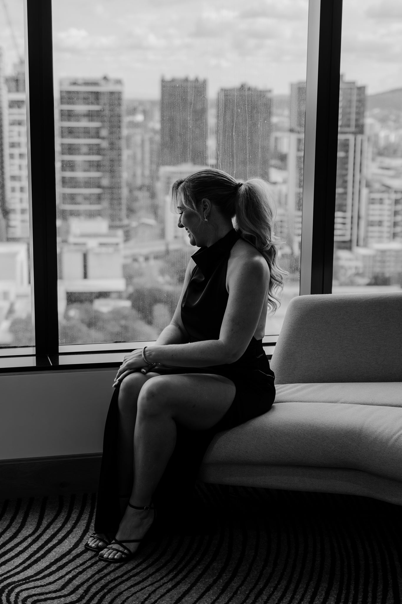 woman in front of windows and city scape in black dress