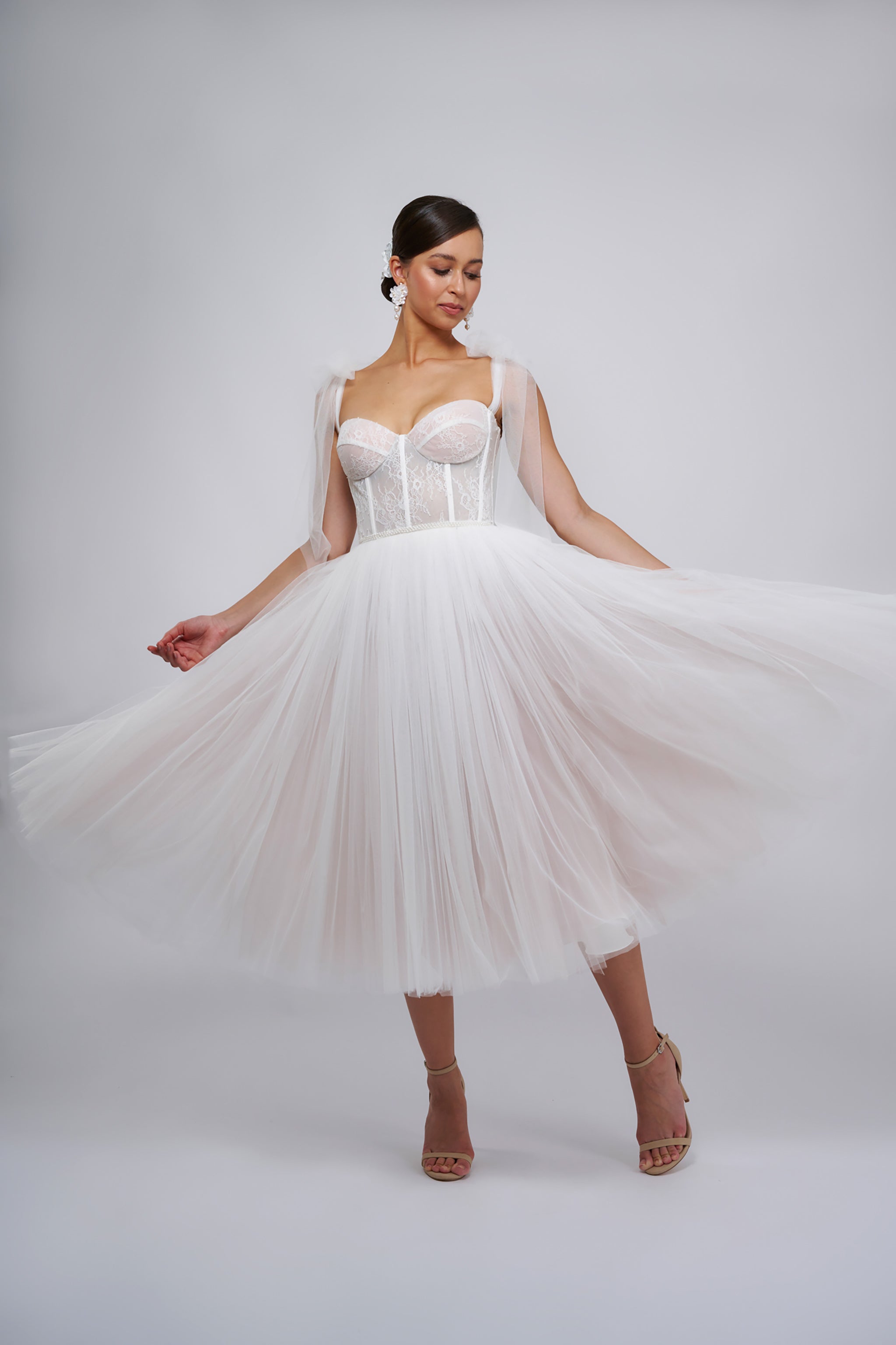 woman in her wedding dress featuring flowing tulle skirt and lace corset with shoulder straps wearing high heel shoes dancing in a white room at her wedding