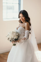 woman in lace wedding dress with outer skirt and sleeves holding bouquet of flowers