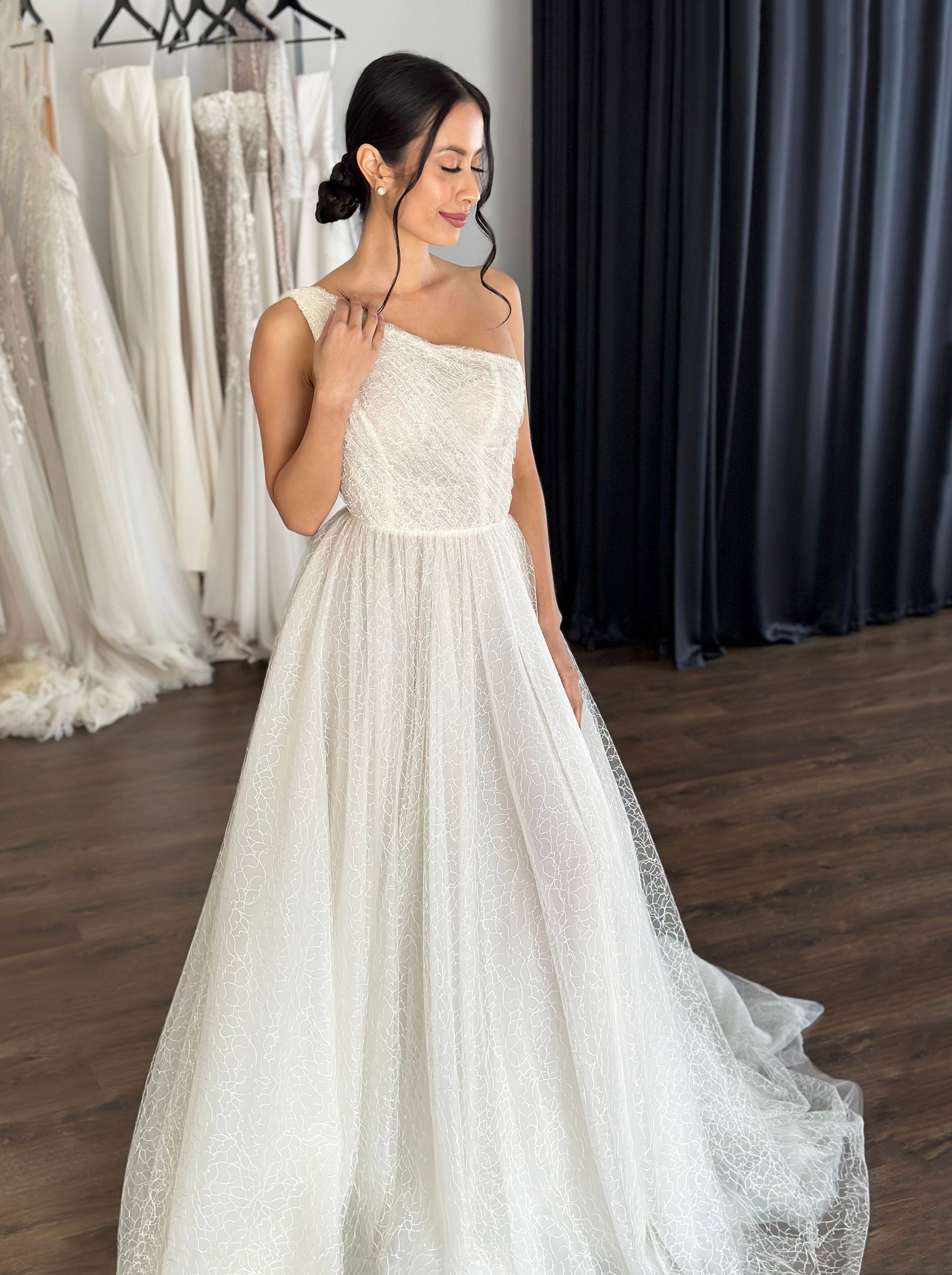 woman posing in embroidered lace wedding dress with one shoulder strap design