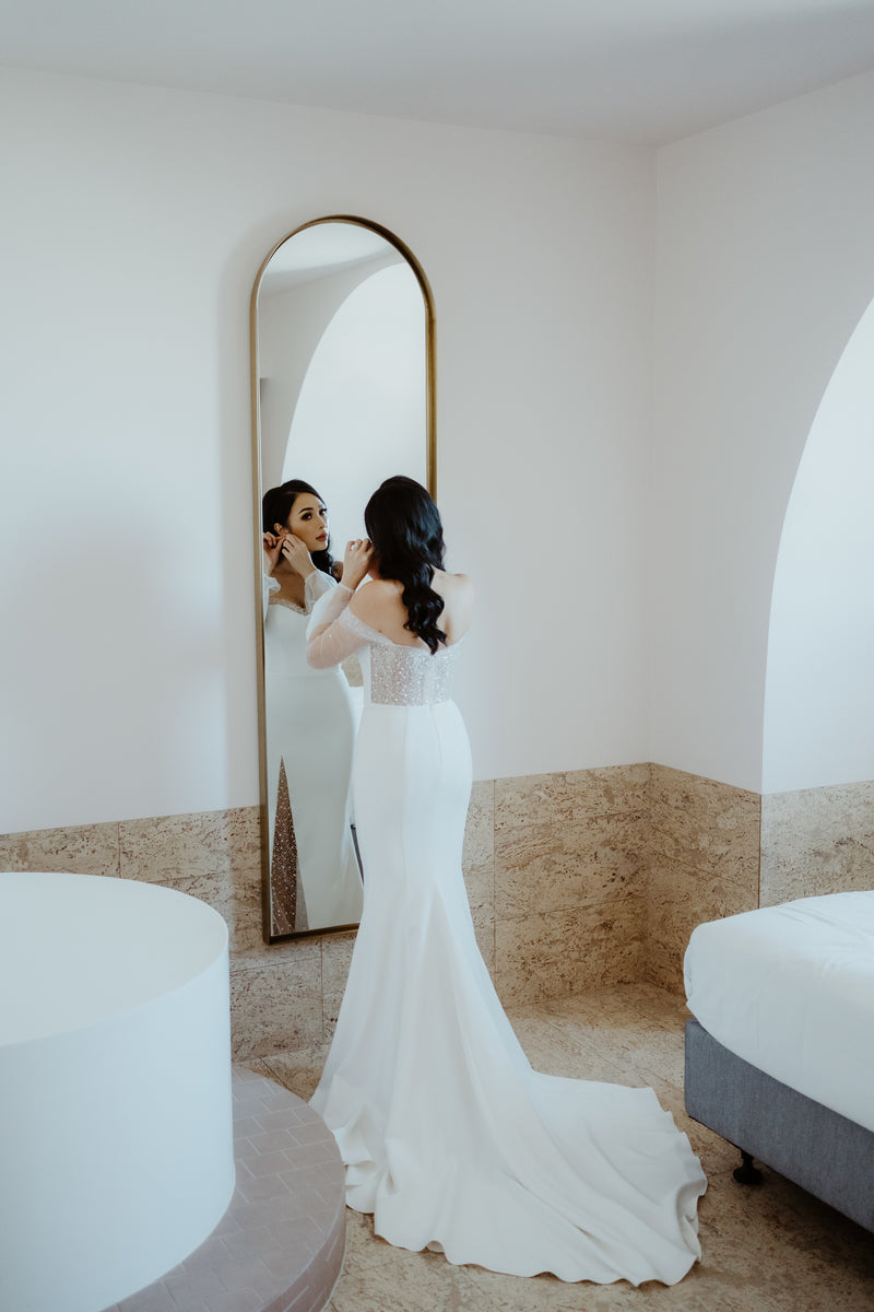 bride fitting into wedding dress in front off mirror and bed