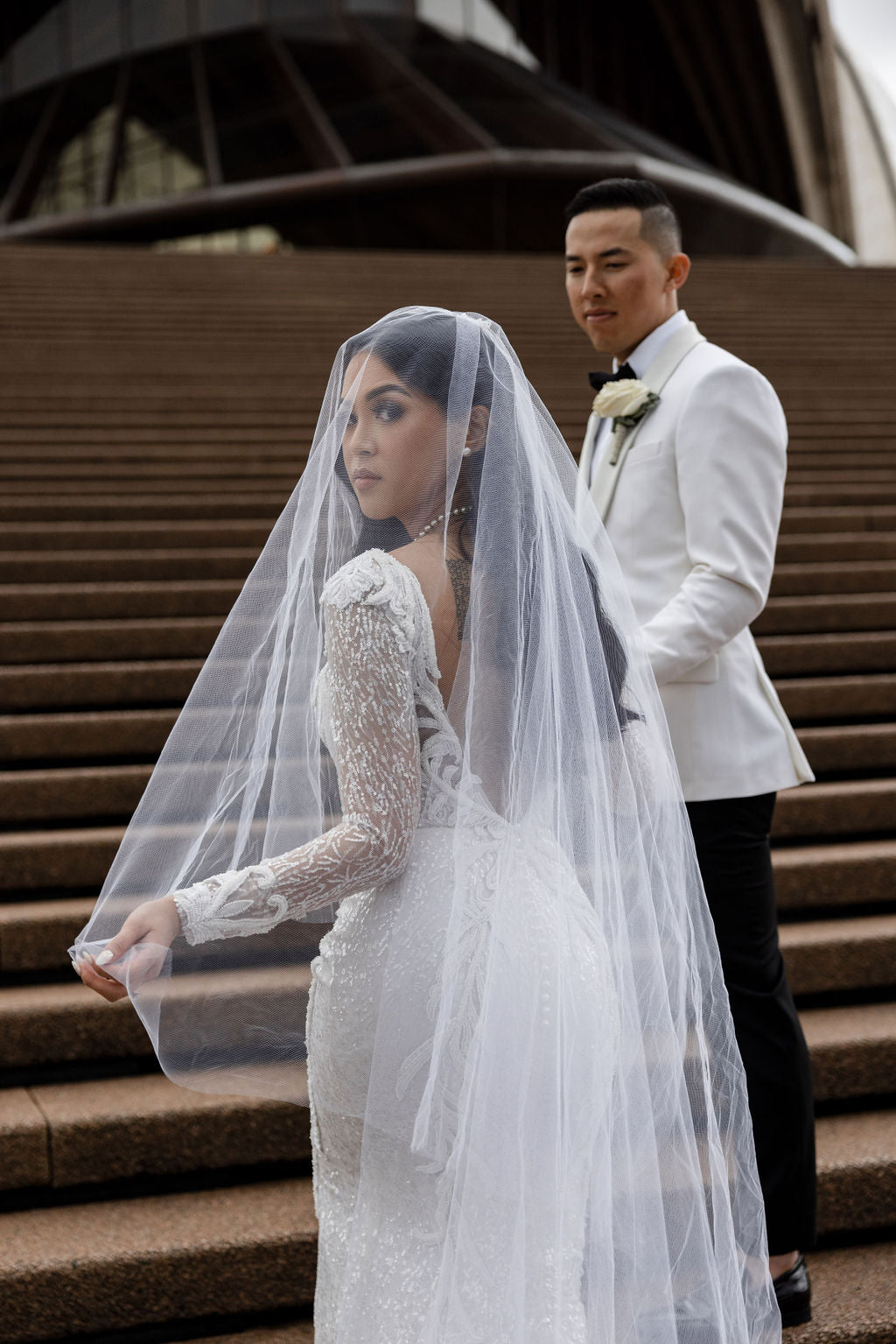 bride in wedding dress and veil holding hands with man in suit on staircase