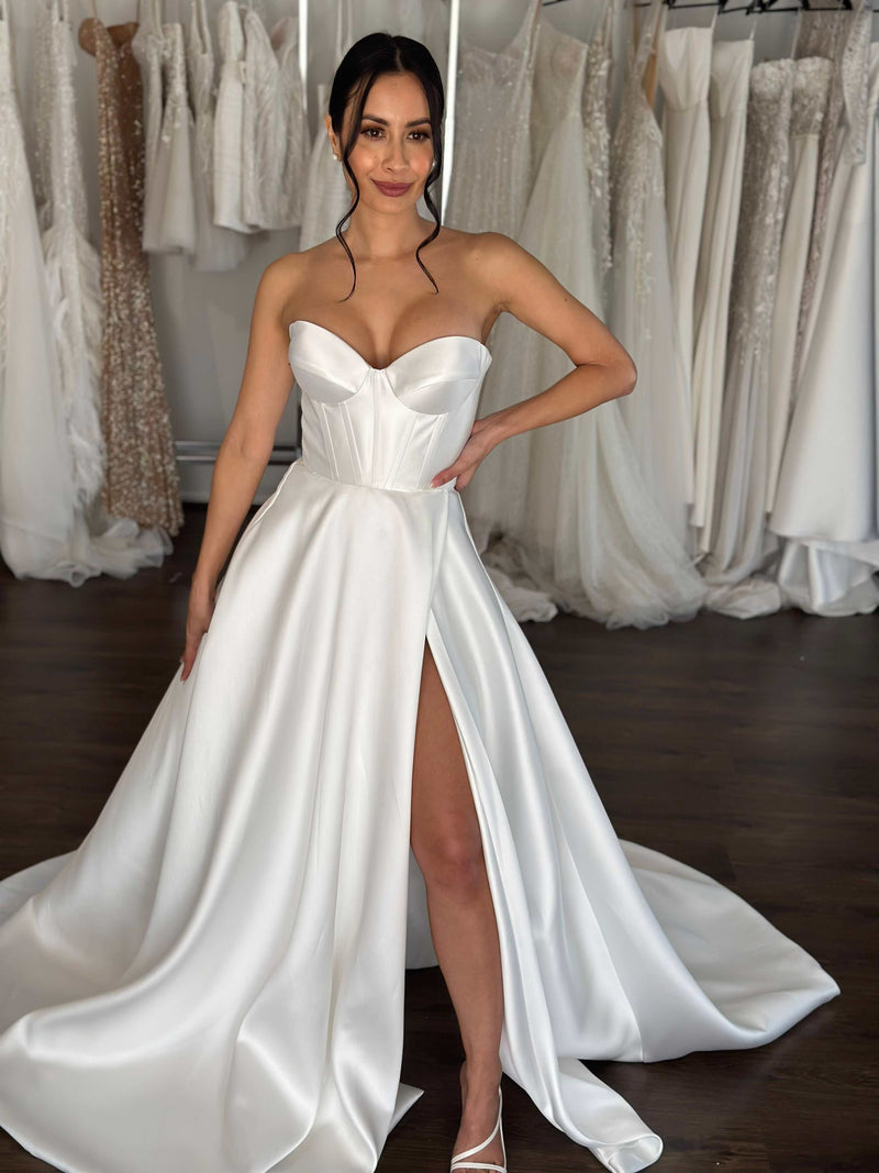 corset wedding dress on woman in front of racks of gowns