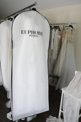 wedding dresses hanging on racks behind bridal garment bag with Euphorie Studios printed on the back of the bag